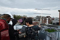 People on a roof wearing tin foil hats try to receive a satellite transmission using an oversized antenna
